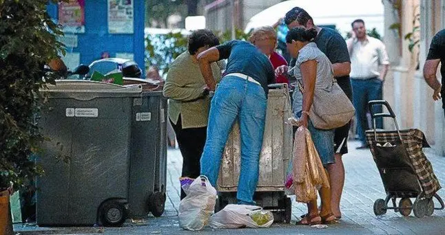 Varias personas cogen comida caducada de un contenedor en la calle de Bail&egrave;n.