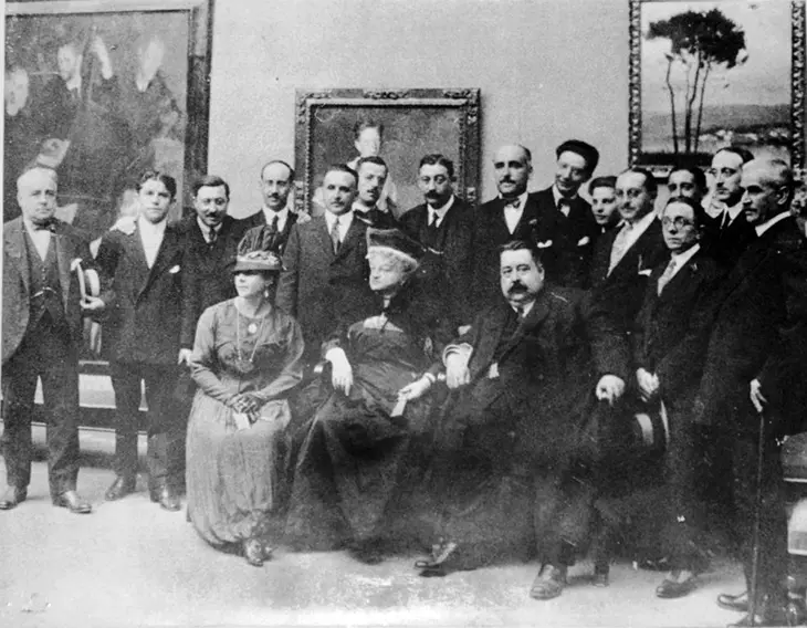Exposici&oacute;n en el Palacio de Mar&iacute;a Pita, en 1917. Est&aacute;n presentes: Tella, Abelenda, Barreiro (en el centro de pie, s&eacute;ptimo comenzando por la izquierda), Sobrino, Palacios, Seijo, Sotomayor, Llor&eacute;ns, Castelao, Concheiro, Franc&eacute;s, Madariaga (con sombrero en las manos), Gonz&aacute;lez del Villar y dos personas sin identificar. Sentados: la mujer de Franc&eacute;s, Emilia Pardo Baz&aacute;n y Picadillo.