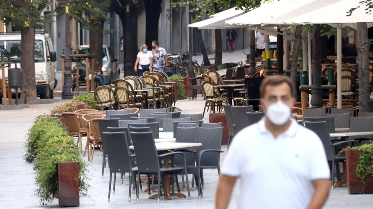 Un hombre caminando cerca de un restaurante en Girona cerrado por las restricciones derivadas de la pandemia. / Twitter.