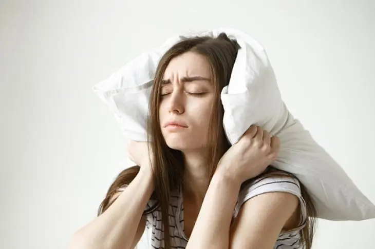 Mujer joven con una almohada cierra los ojos. / Freepik.
