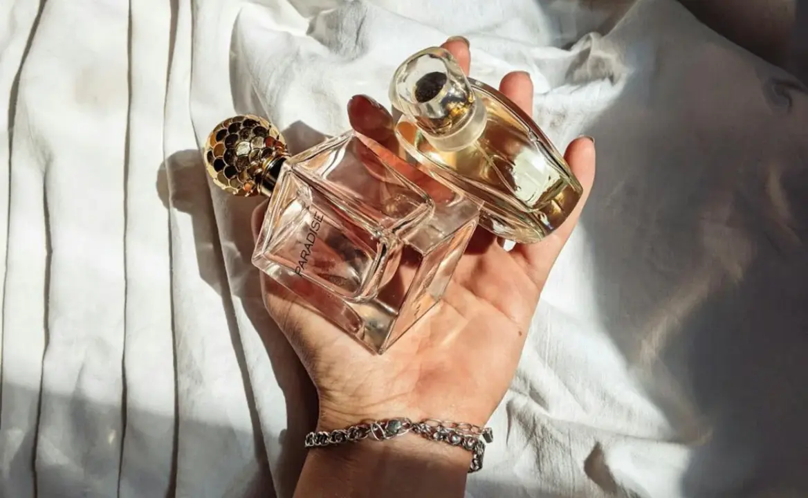 Mano sosteniendo dos botellas de cristal que contienen fragancia.
