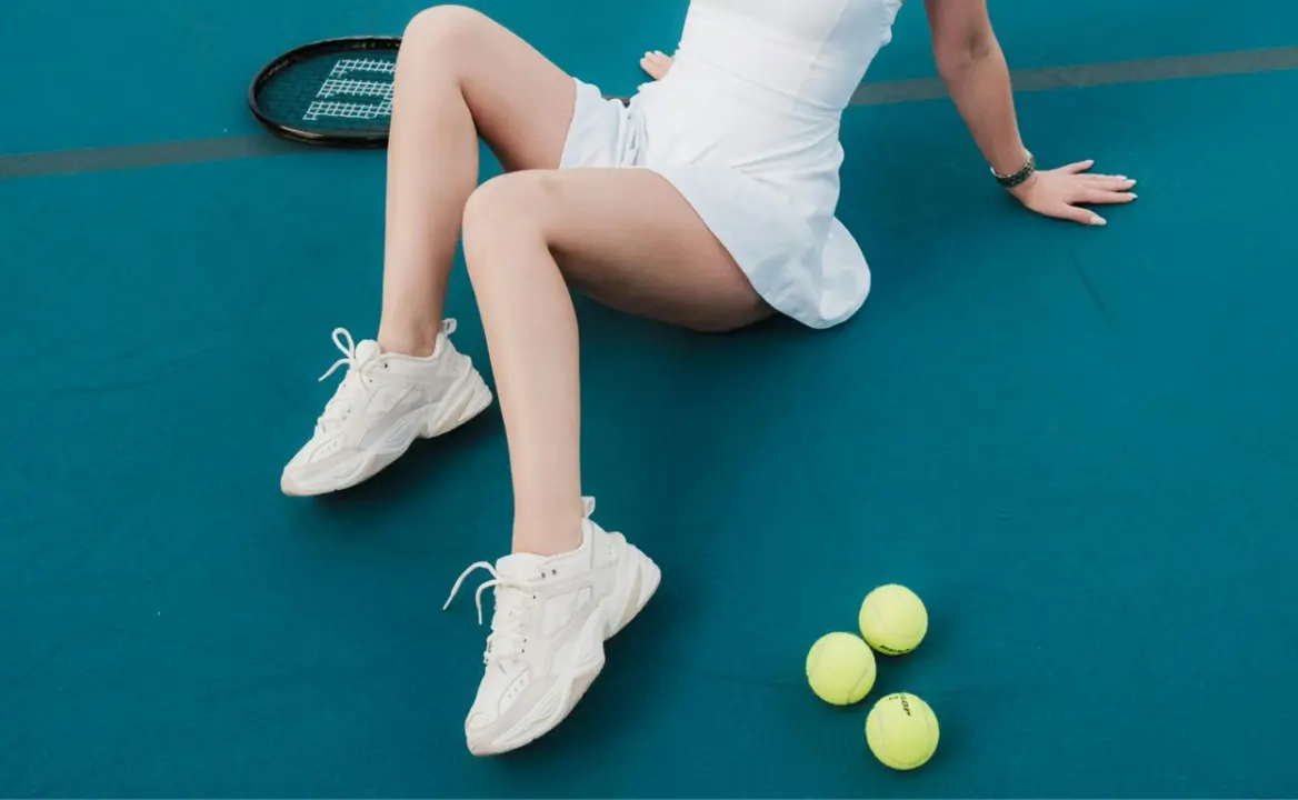 Mujer con tenis blancos en cancha de tenis.
