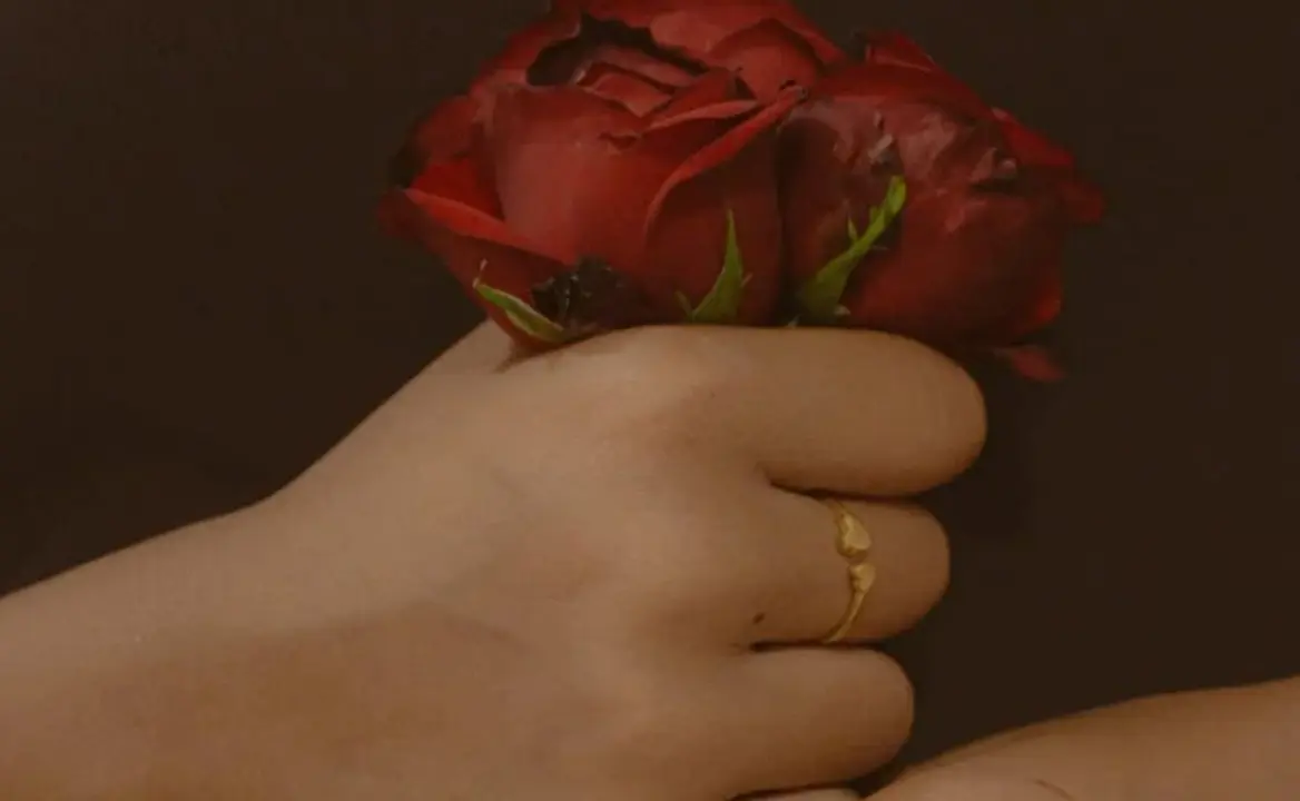 Mano con anillo en el dedo y flor roja.