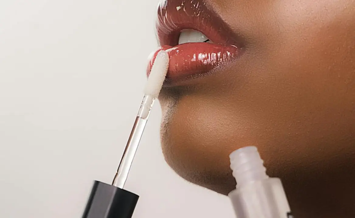 Mujer con gloss en los labios y envase del producto. 
