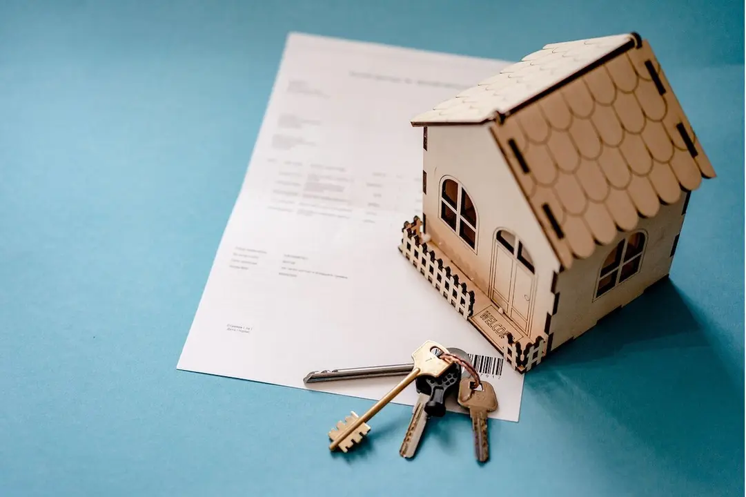 Casa en miniatura sobre un contrato y unas llaves al lado.