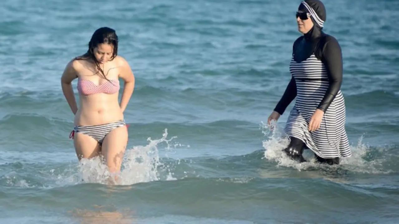 Una mujer en bikini y otra en burkini. / @inter_pl