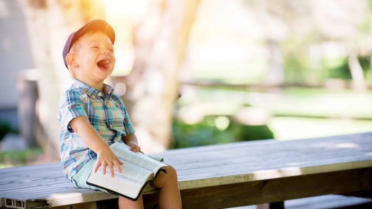 Ni&ntilde;o riendo con un libro sobre las rodillas. / Ben White. / Unsplash