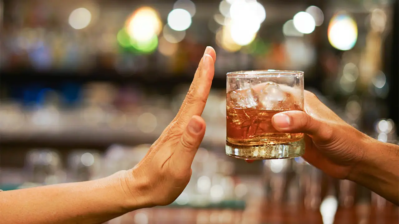 Una mano en se&ntilde;al de detente mientras otra mano le ofrece un vaso con alcohol. / Pixabay