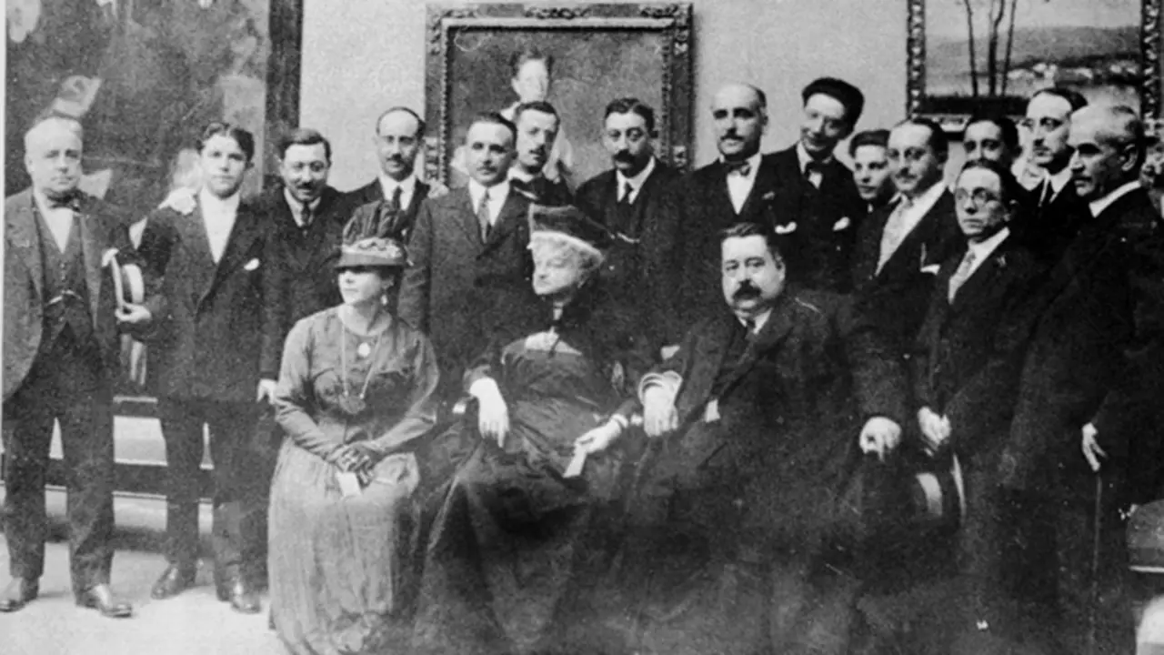 Exposici&oacute;n en el Palacio de Mar&iacute;a Pita, en 1917. Est&aacute;n presentes: Tella, Abelenda, Barreiro (en el centro de pie, s&eacute;ptimo comenzando por la izquierda), Sobrino, Palacios, Seijo, Sotomayor, Llor&eacute;ns, Castelao, Concheiro, Franc&eacute;s, Madariaga (con sombrero en las manos), Gonz&aacute;lez del Villar y dos personas sin identificar. Sentados: la mujer de Franc&eacute;s, Emilia Pardo Baz&aacute;n y Picadillo.
