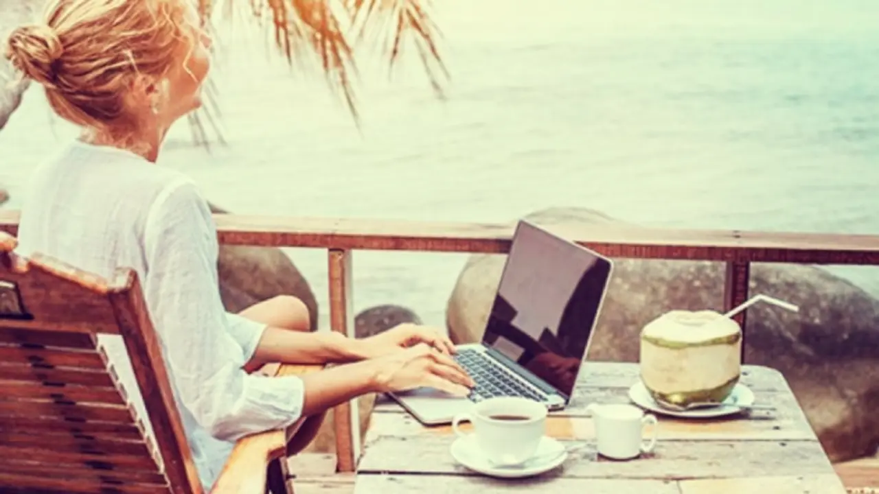 Un mujer utilizando una laptop a la orilla del mar. Pexels.
