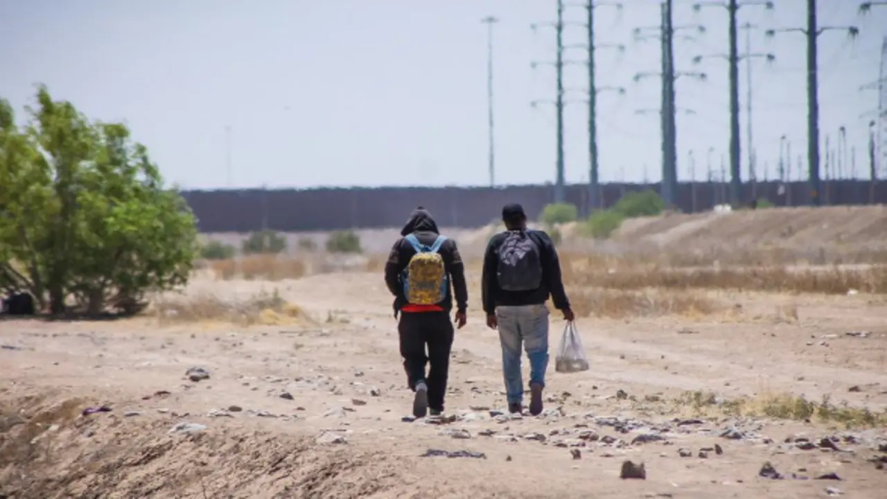 Dos hombres caminan junto al muro fronterizo que divide M&eacute;xico de Estados Unidos. / OIM.