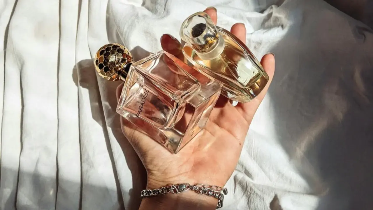 Mano sosteniendo dos botellas de cristal que contienen fragancia.