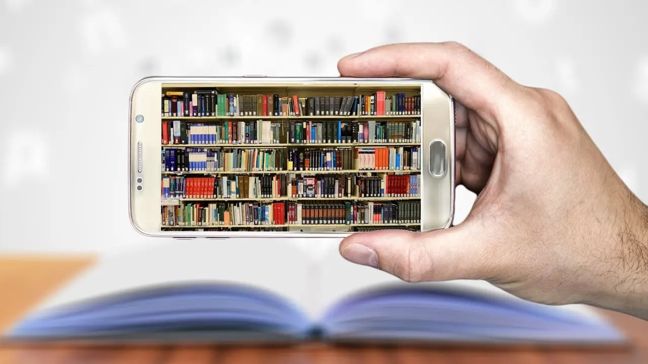 Una mano sostiene un m&oacute;vil que muestra una imagen de una biblioteca. / RR SS.