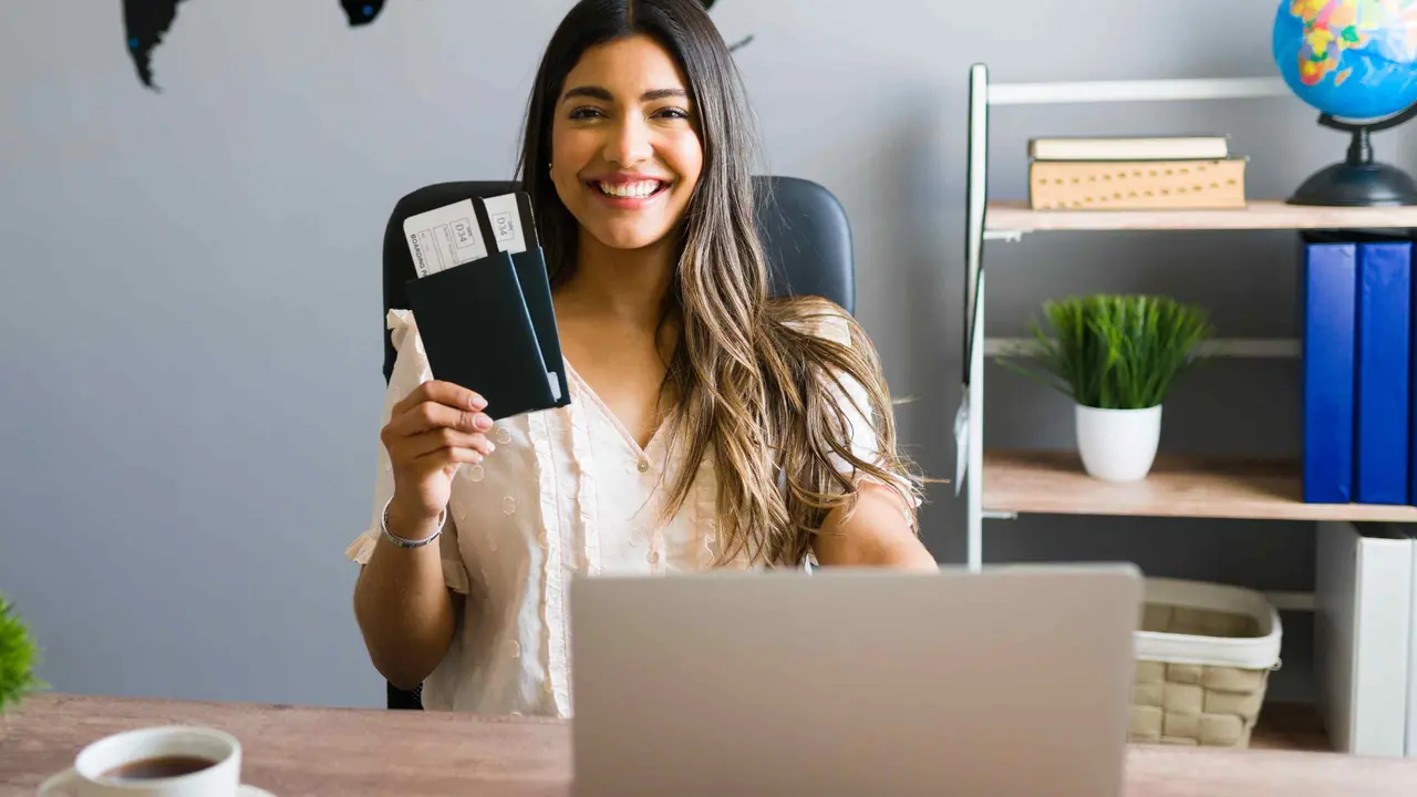I am here to help you with your booking and travel questions. Female sales agent holding plane tickets while smiling and making eye contact at the travel agency