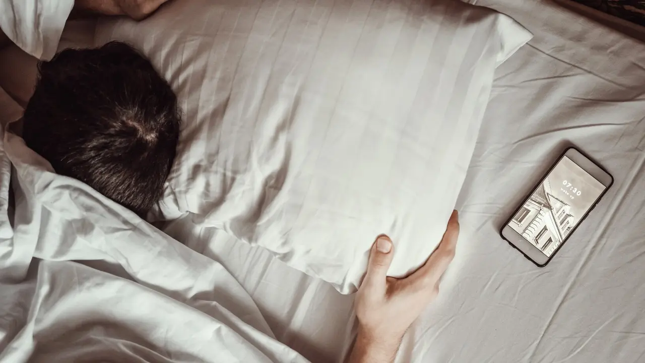 Una persona duerme en a cama con su m&oacute;vil. / Freepik.